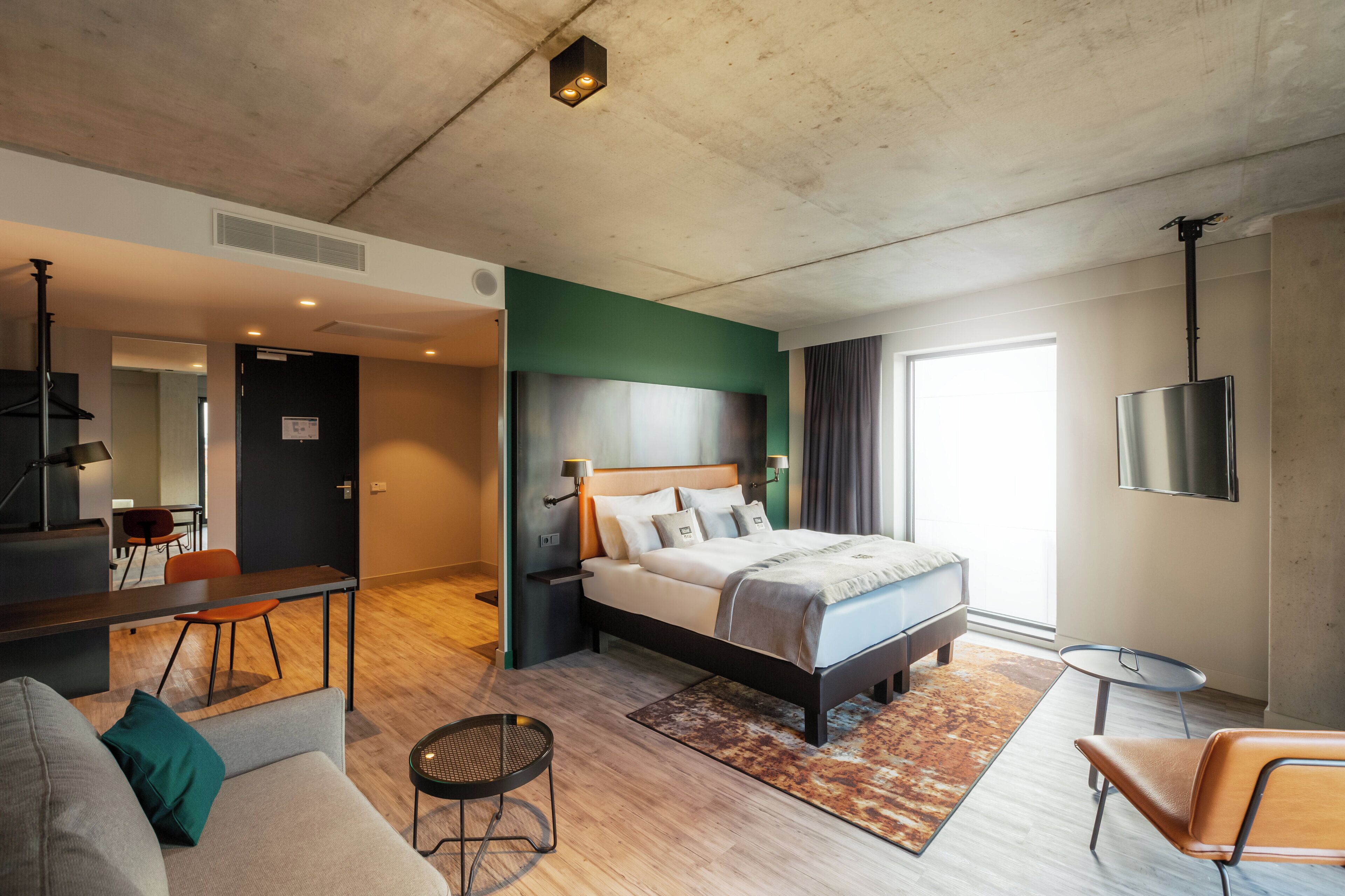 A modern hotel room with a bed, a sofa, a small table, and a TV.