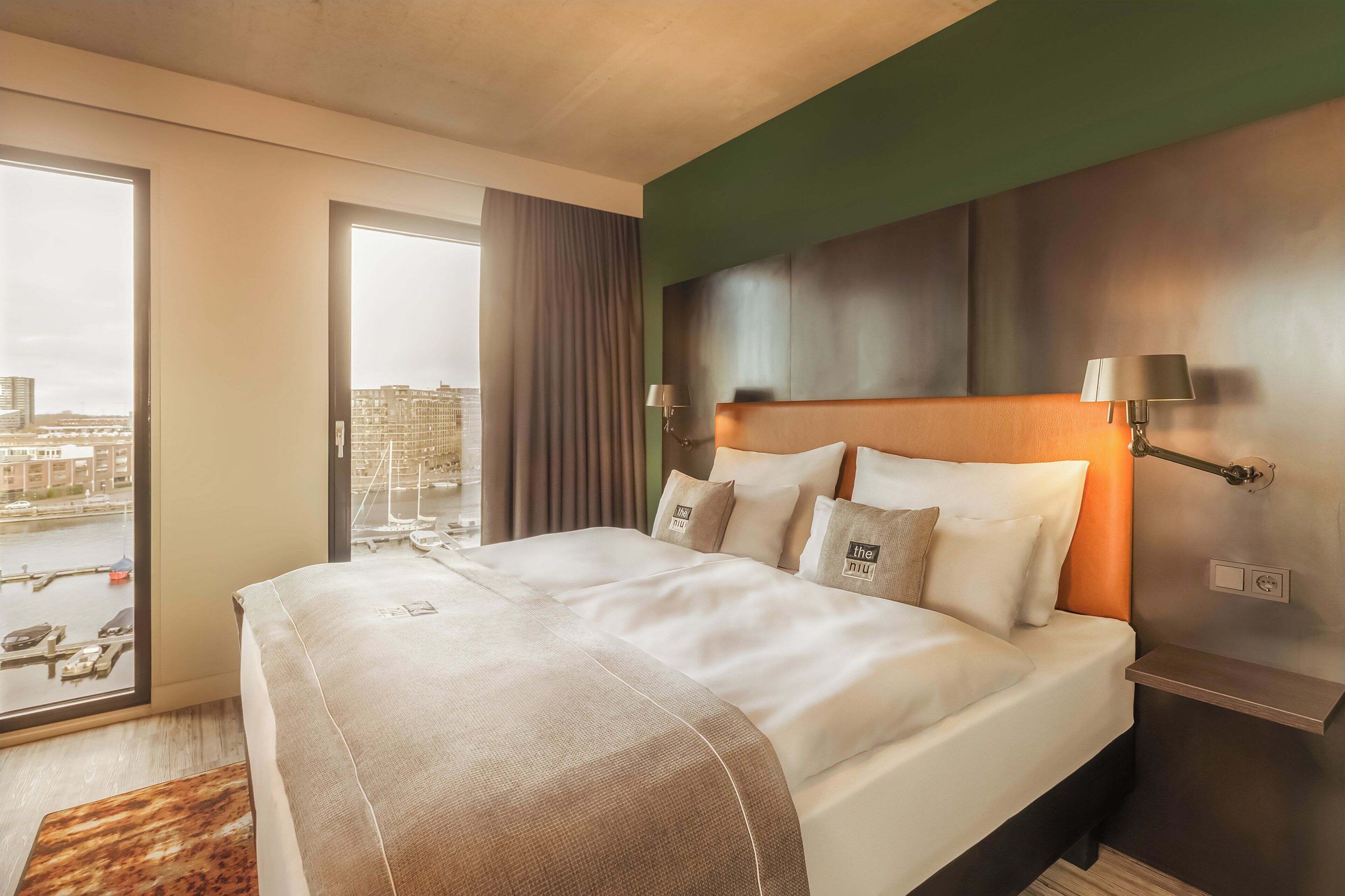 A modern hotel room with a large bed, city view, and a green accent wall.