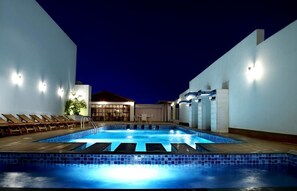 A swimming pool with lounge chairs and a building in the background. - Ista Suites Seef (Manama)