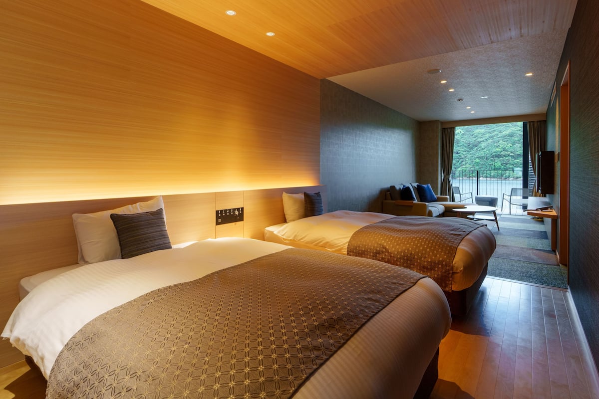 A hotel room with two beds, a seating area with a table, and a view of the outdoors.