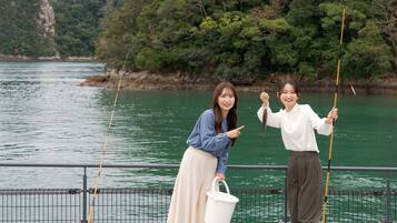 Two people fishing by a railing with a body of water and trees in the background.