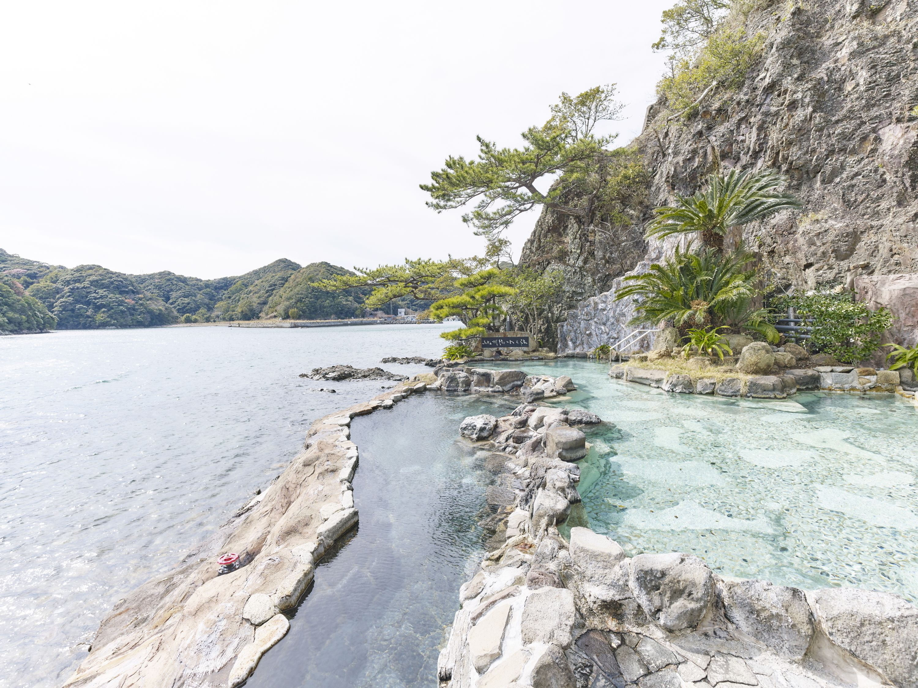 A coastal landscape with clear waters, rocky formations, and lush greenery.