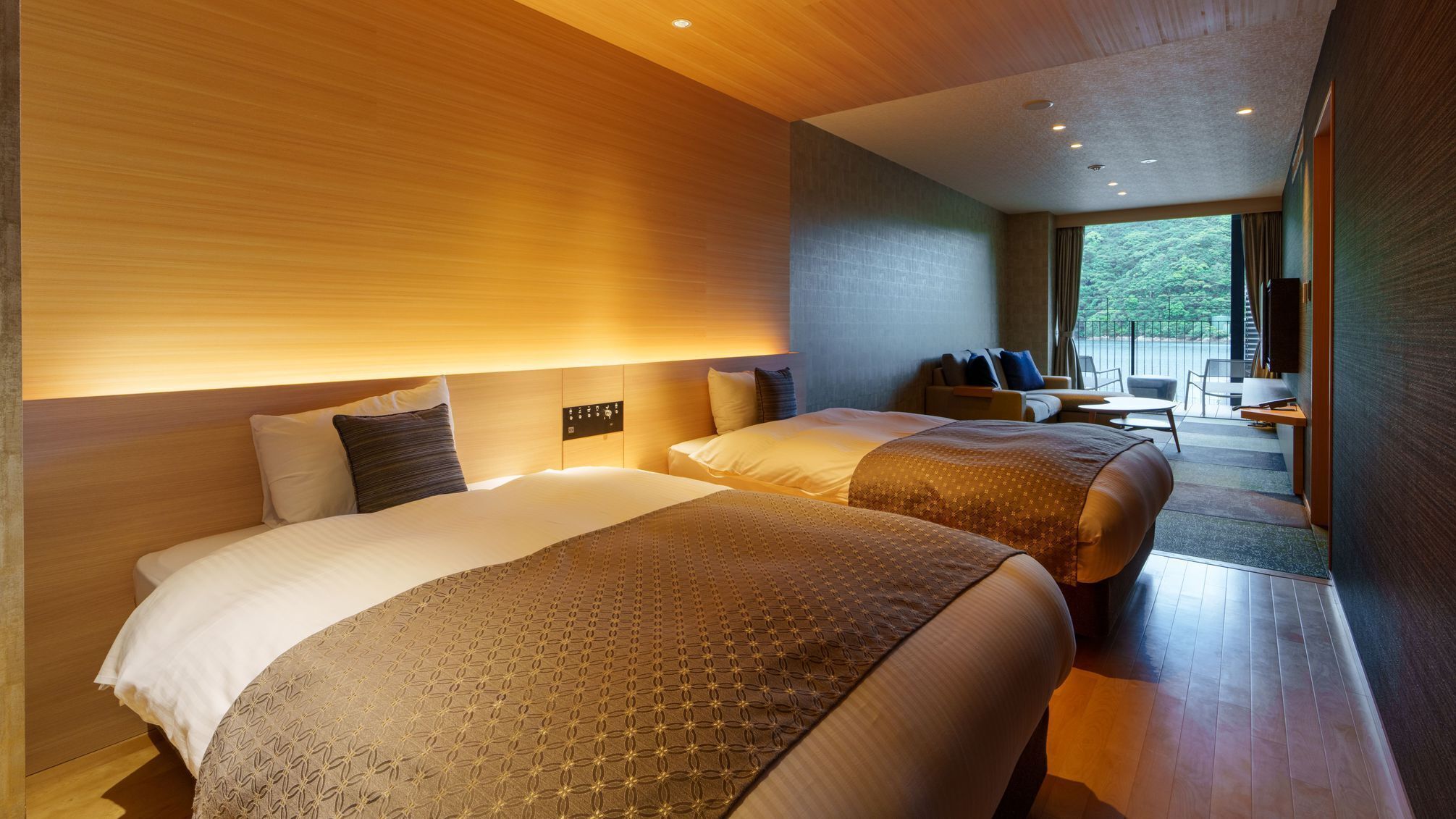 A modern hotel room with two beds, a sofa, a desk, and a balcony with a view.