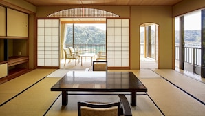 A traditional Japanese room with tatami flooring, a low table, and sliding doors leading to a balcony with a mountain view. - Kumano-bettei Nakanoshima (Nachikatsuura)