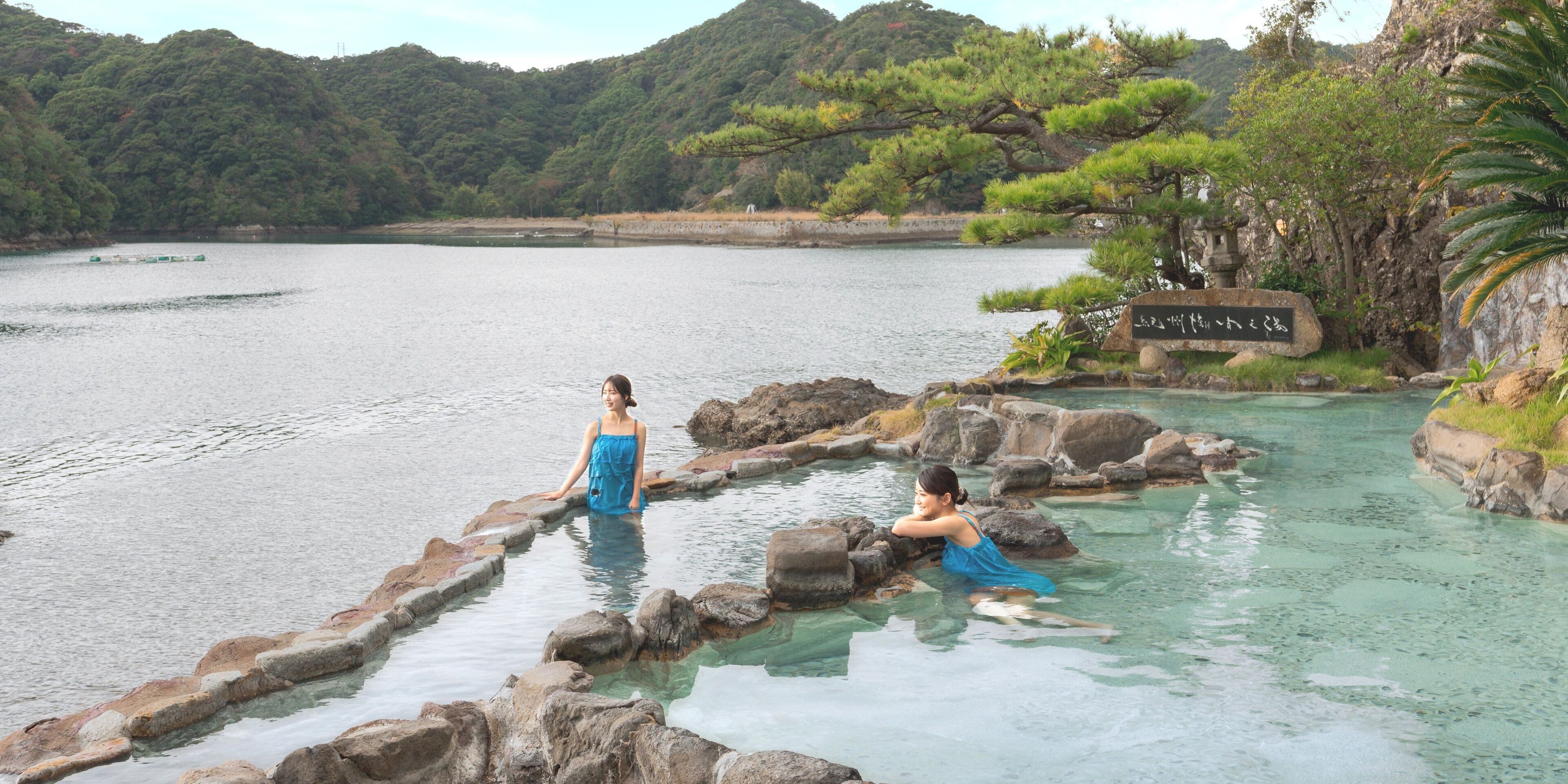 Two women in a natural setting with a body of water and rocky terrain.