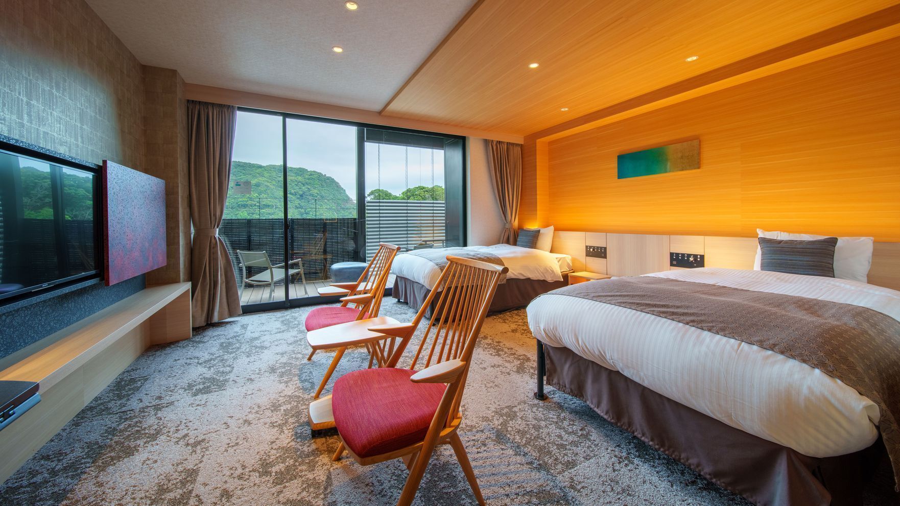 A hotel room with a large bed, a TV, a seating area with chairs, and a balcony with a view.