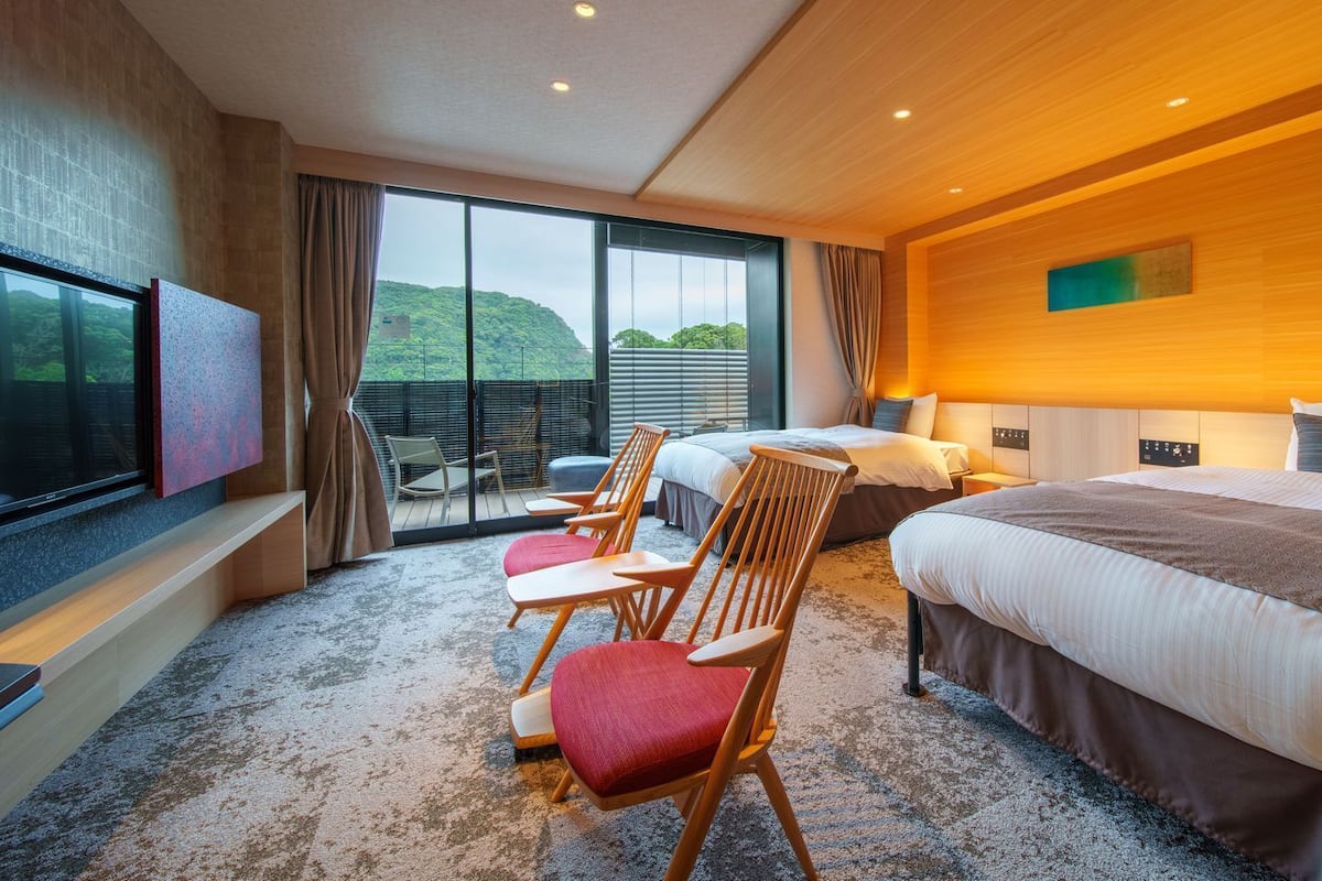 A hotel room with a large bed, a TV, a seating area with chairs, and a balcony with a view.