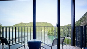 A balcony with two chairs and a table, overlooking a body of water and greenery. - Kumano-bettei Nakanoshima (Nachikatsuura)