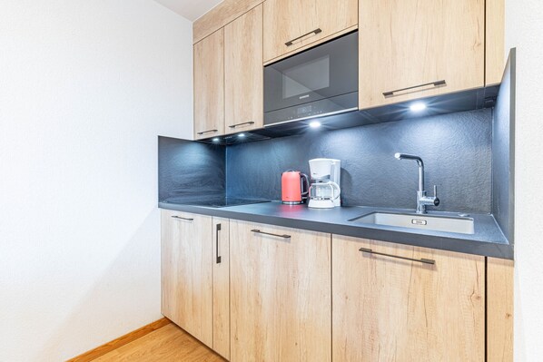 A modern kitchen with wooden cabinets, a black countertop, a coffee maker, and a sink.