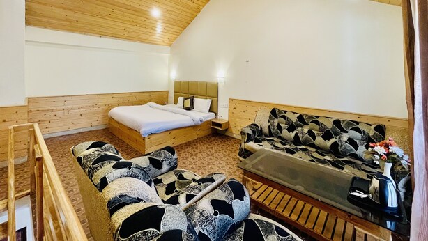 Ein gemütliches Zimmer mit Holzbalkendecke, einem Bett, einem Sofa und einem kleinen Tisch mit Blumen in einer Vase.