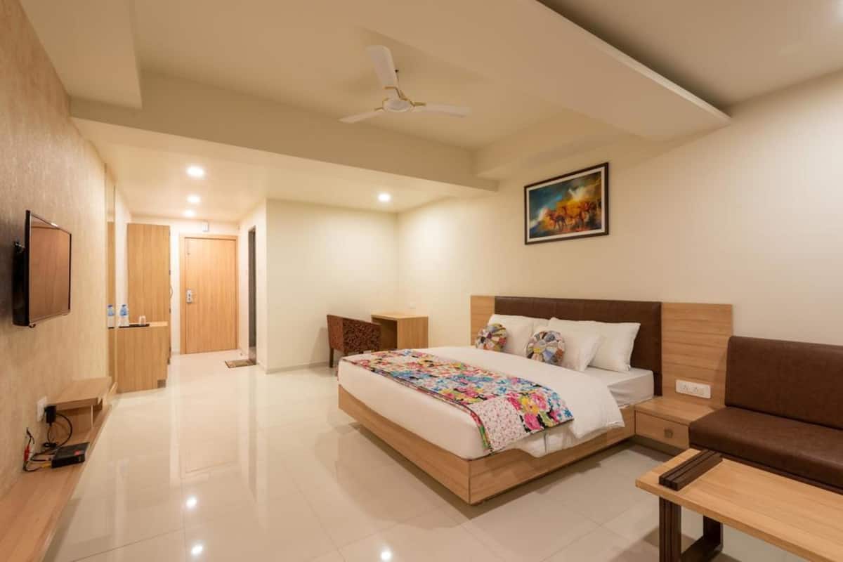 A modern hotel room with a large bed, bedside tables, a sofa, a TV, and a ceiling fan.