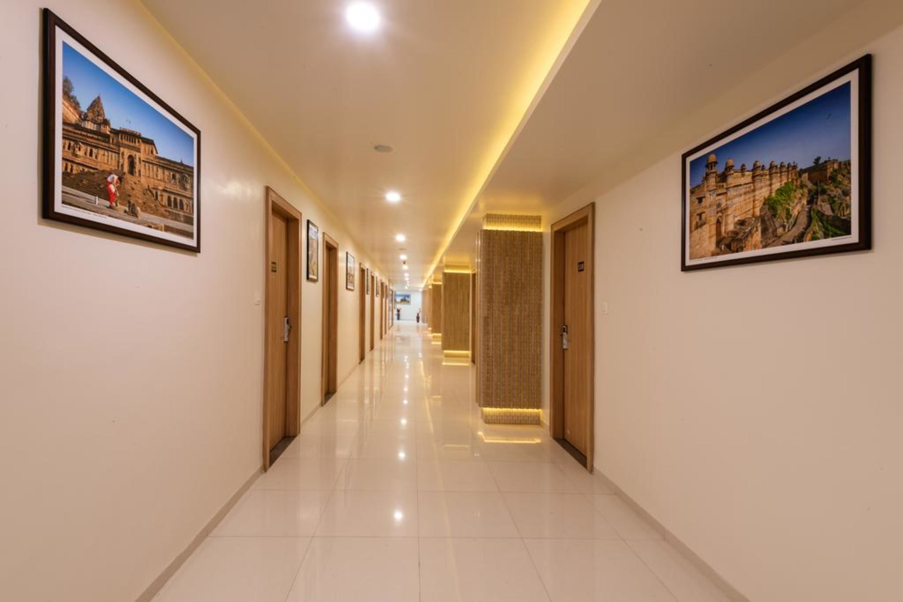 A hotel hallway with framed pictures on the walls, doors on either side, and a shiny tiled floor.