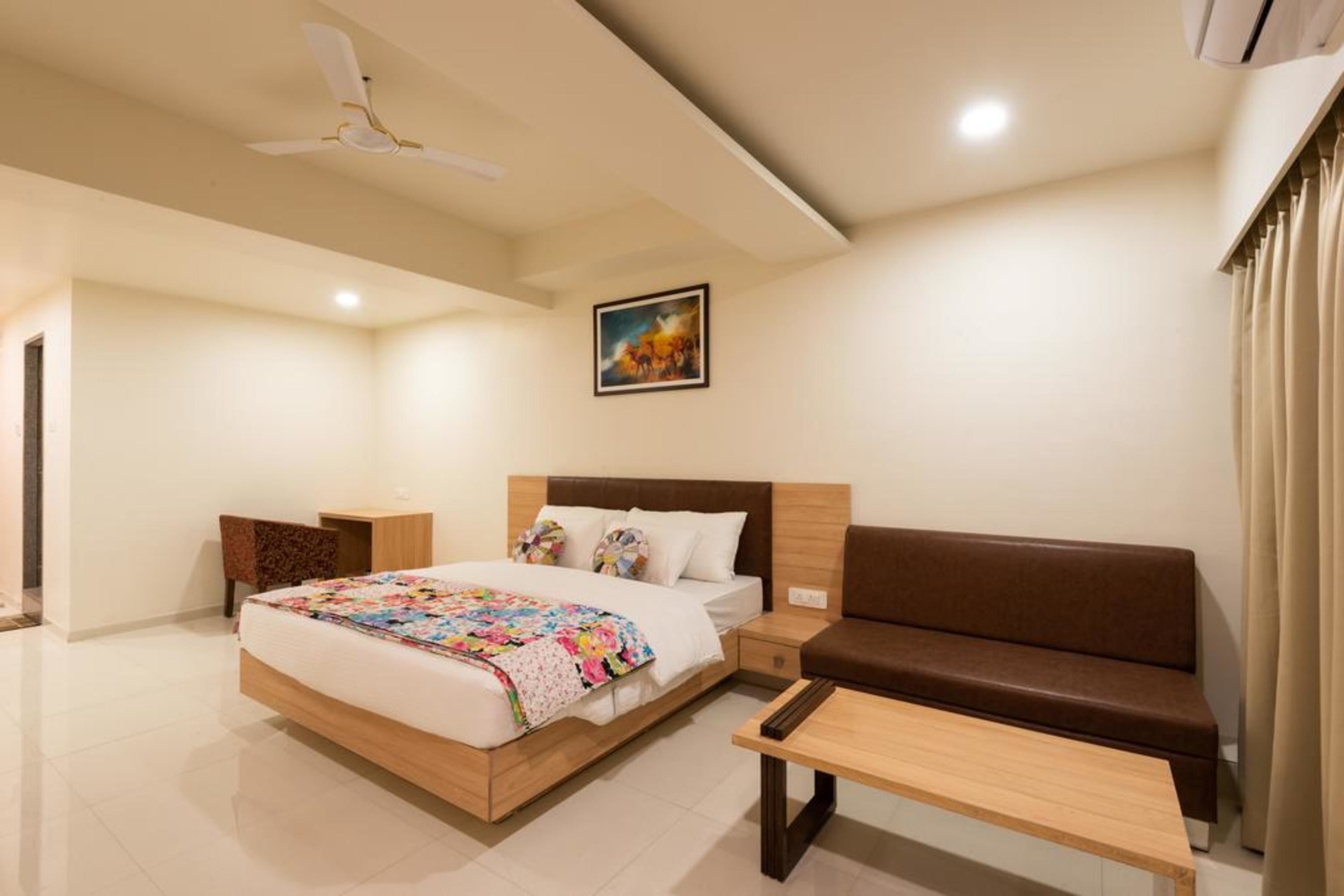 A modern hotel room with a bed, a sofa, a small table, and a ceiling fan.