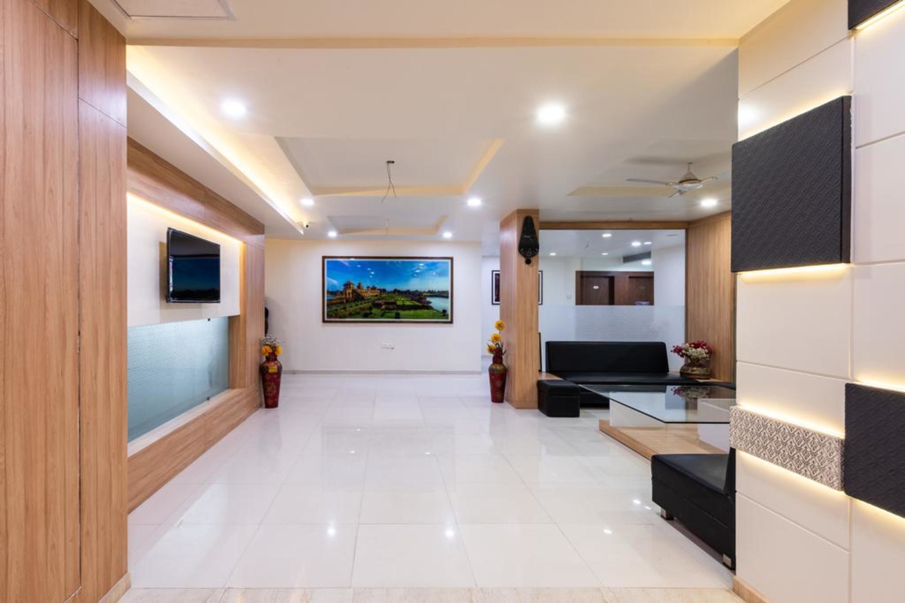 A modern hotel lobby with a flat-screen TV, a large landscape painting, a reception desk, and a seating area.