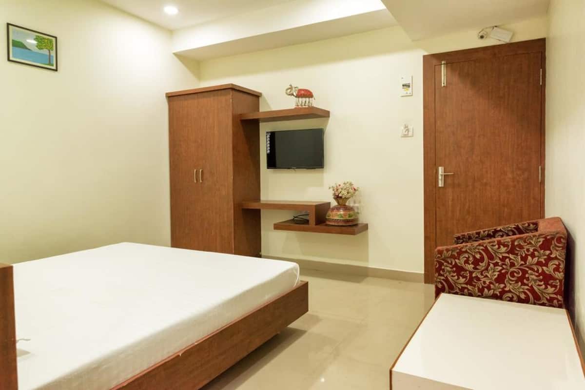 A bedroom with a bed, a wardrobe, a TV mounted on the wall, and a small shelf with decorative items.