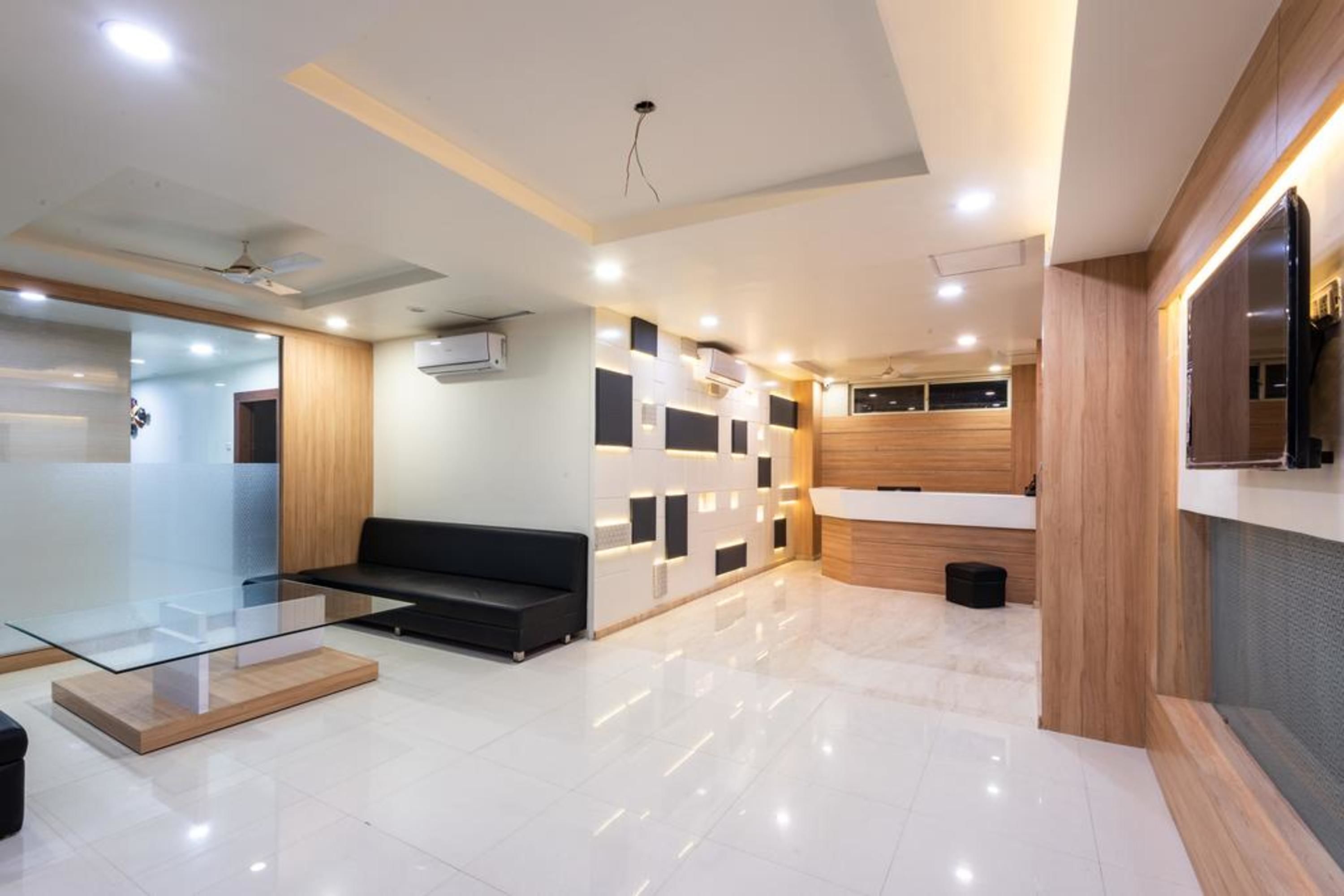 Un moderno vestíbulo de hotel con una mesa de centro de vidrio, un sofá negro, una recepción y una pared decorativa de madera.
