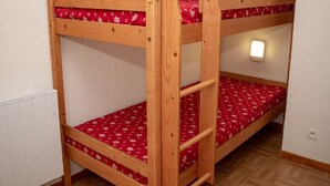 Un lit superposé avec un matelas à motifs rouges, une structure en bois et un luminaire fixé au mur.