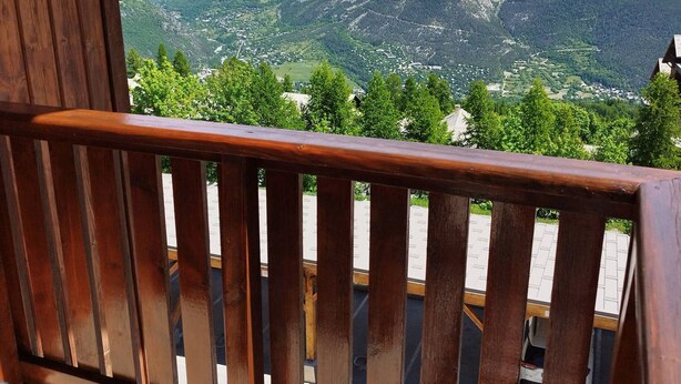 Une balustrade en bois surplombe un paysage montagneux, avec un village situé en contrebas.