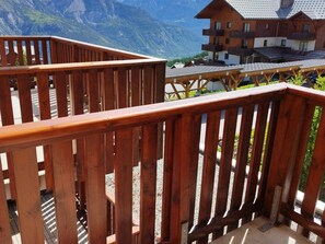 A wooden balcony with a mountain view, a building with multiple balconies, and a gravel ground. - Studio 4 People with Balcony and Parking, Puy-Saint-Vincent (Puy-Saint-Vincent)