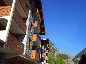 A multi-story building with balconies, stone walls, and a mountainous backdrop.