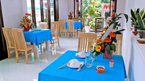 Un comedor con mesas preparadas para dos, con manteles azules, sillas de madera y centros de mesa florales.