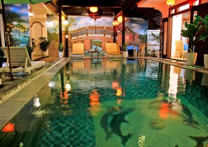 An indoor swimming pool with clear water, a mural of a traditional building, and several lounge chairs. - Green Island Hoian Villa (Da Nang)