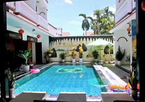 A swimming pool with a tiled deck, surrounded by potted plants and a decorative wall. - Green Island Hoian Villa (Da Nang)