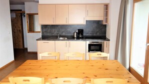 A compact kitchen with wooden cabinets, a black countertop, and a dining table with four chairs. - Pracondu 1 002 - OUTDOOR & FUN  charming apartment (Haute-Nendaz)