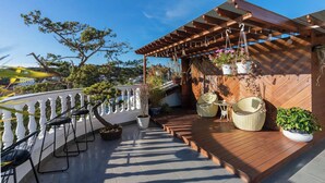 A wooden deck with outdoor seating, potted plants, and hanging flower baskets. - N Queen Apartment Hotel (Xuan Huong - Da Lat)