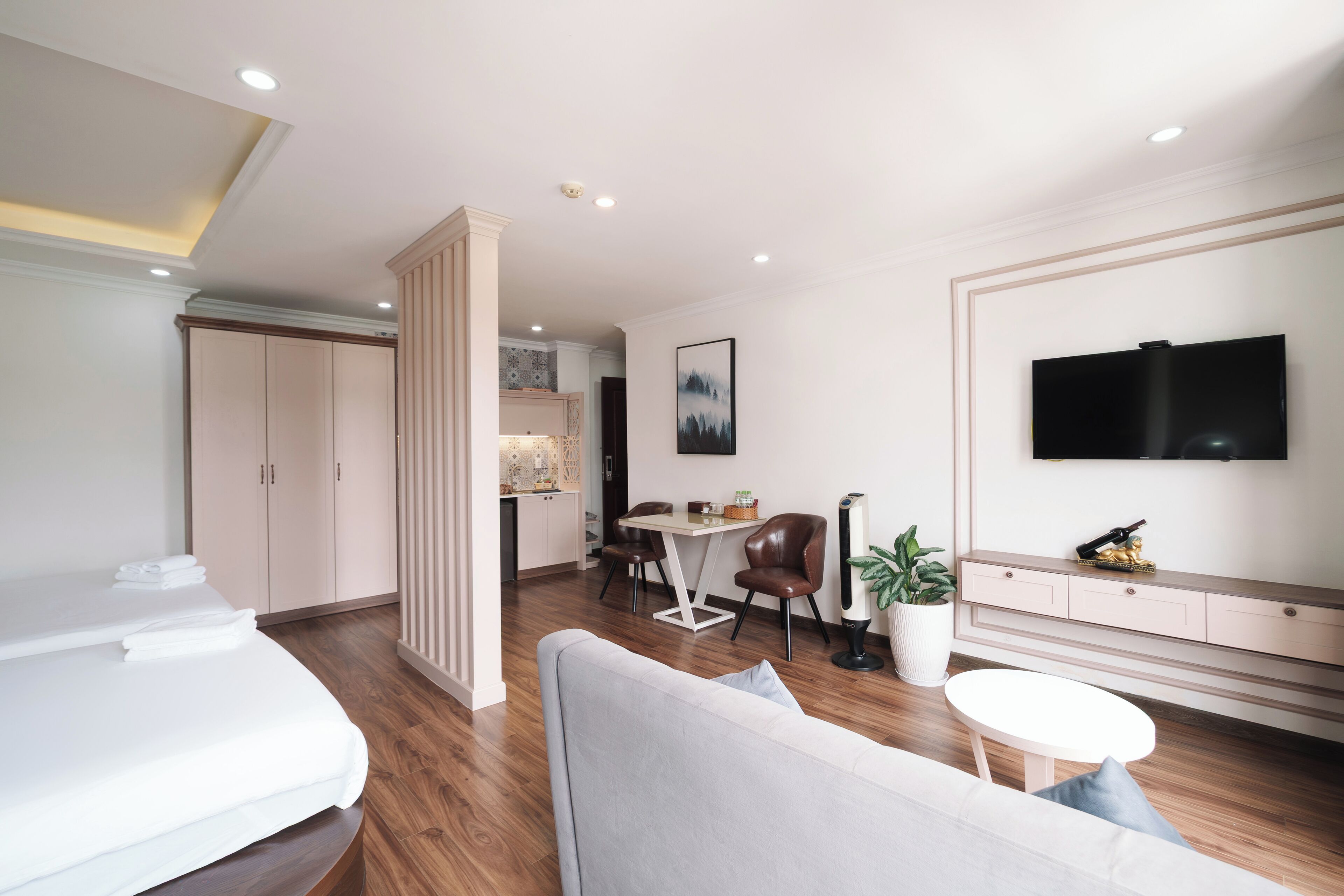 Ett modernt hotellrum med en säng, en soffa, en matplats med stolar, en tv som är monterad på väggen och ett litet bord.