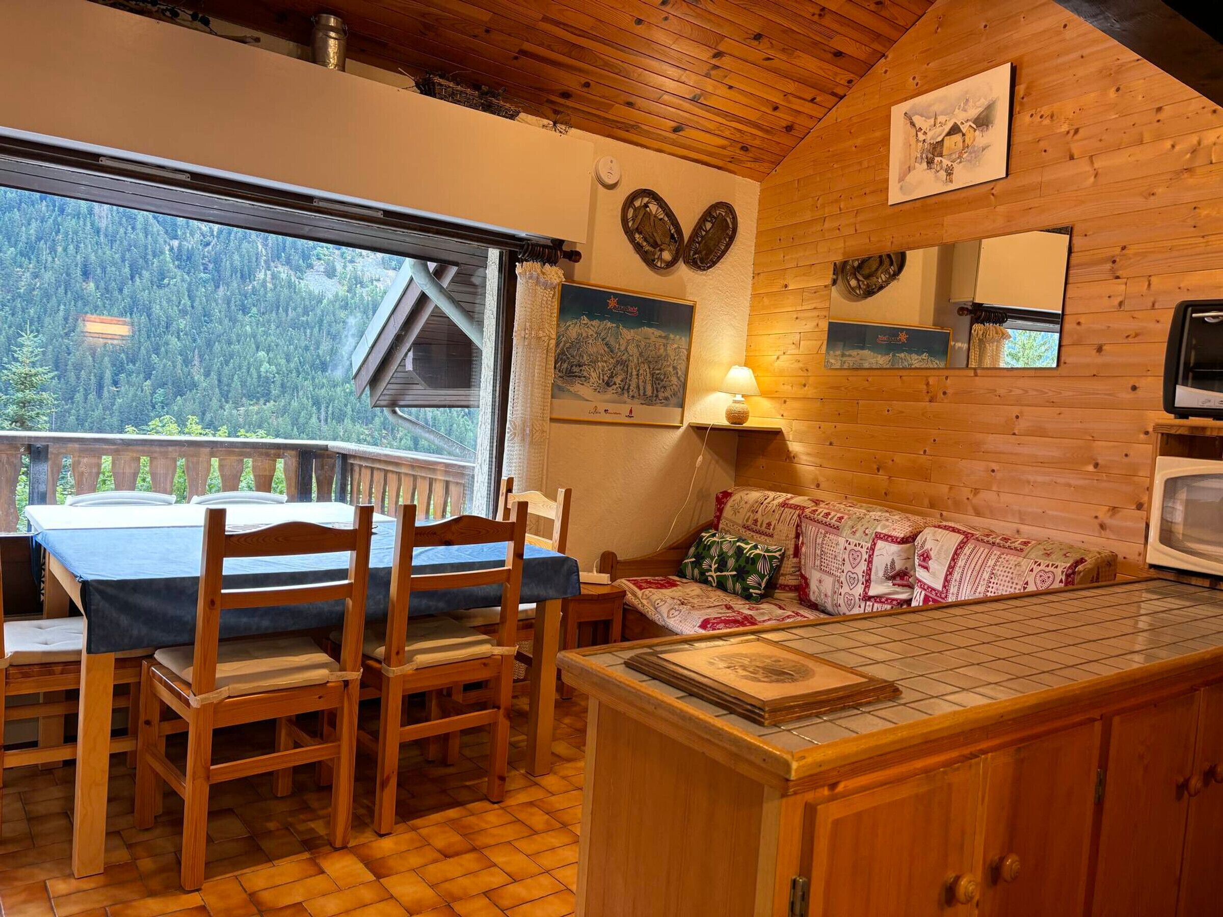 Ein gemütliches Blockhäuschen-Interieur mit Essbereich, Holzmöbeln, einer Couch mit gemusterten Kissen und einem Fernseher.