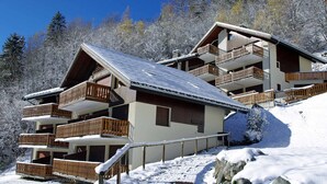 Una chaleta de varios pisos con balcones de madera, un camino de entrada empinado y paisajes nevados.