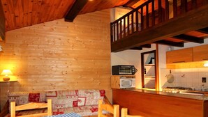 Interior acogedor de una cabaña con una mesa de comedor de madera, un banco y una pequeña cocina con microondas y estufa.