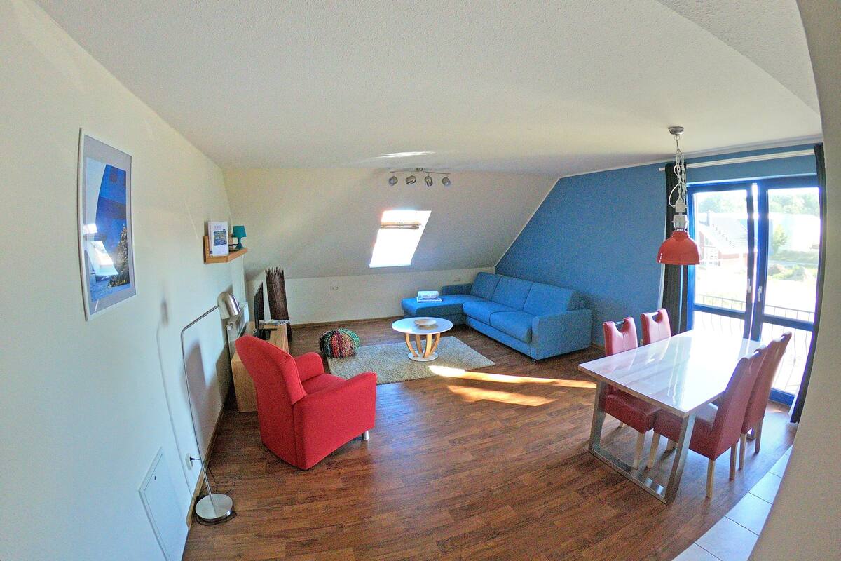 A modern living room with a blue sofa, red armchair, and a dining table with chairs.