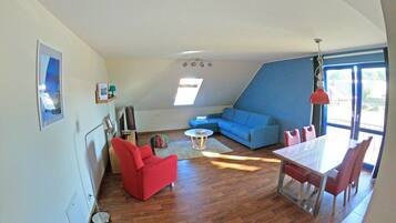 Ein modernes Wohnzimmer mit einem blauen Sofa, einem roten Sessel und einem Esstisch mit Stühlen.
