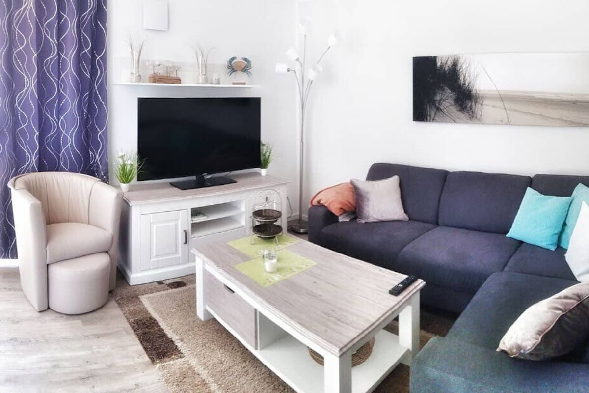 A modern living room with a grey sofa, a white coffee table, a beige armchair, and a flat-screen TV on a white cabinet.