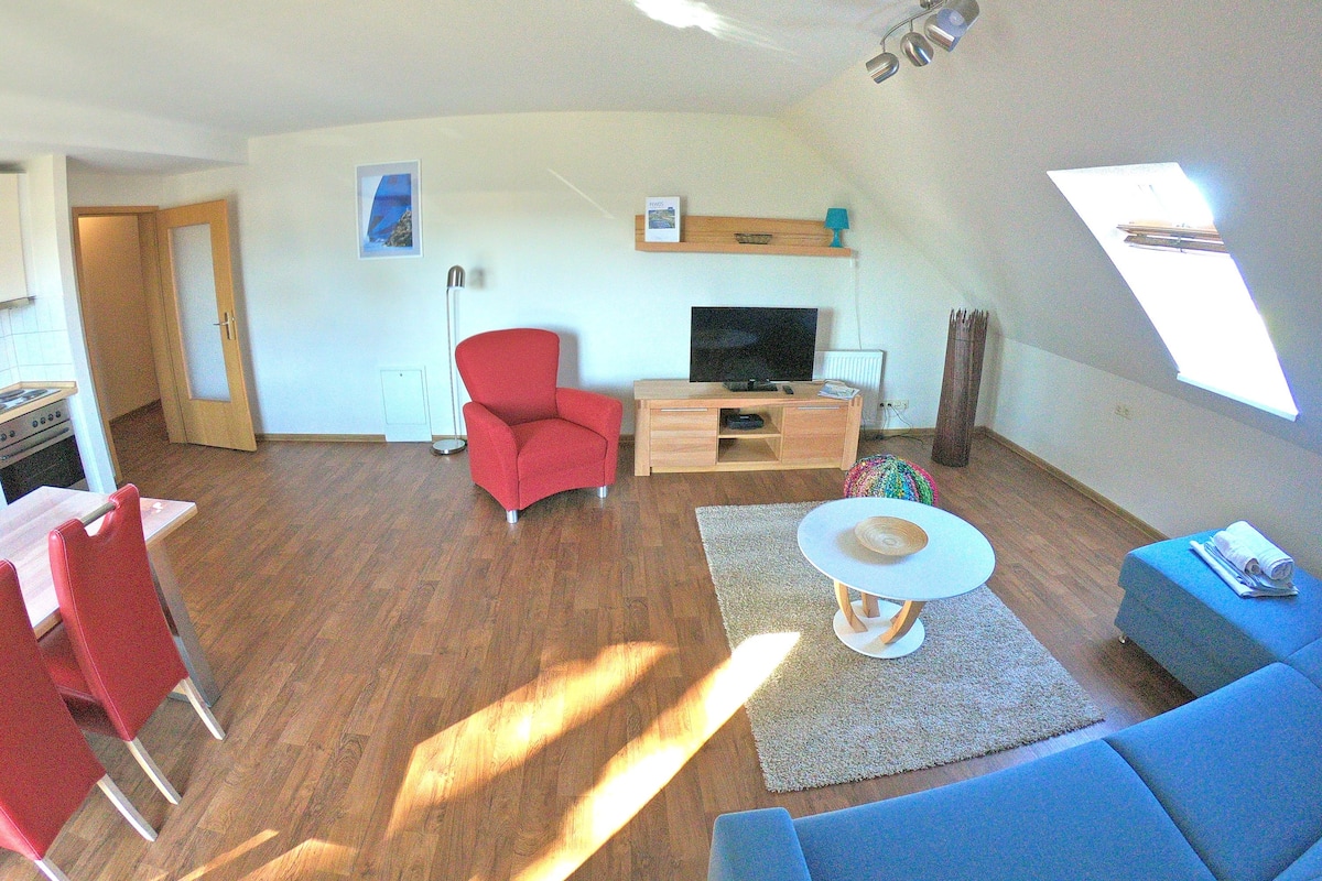A compact living space with a dining area, a red armchair, a TV, and a sofa.