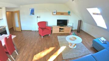 A compact living space with a dining area, a red armchair, a TV, and a sofa.
