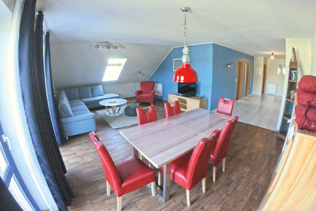 A dining area with a wooden table and red chairs, a blue sofa, and a red pendant light.