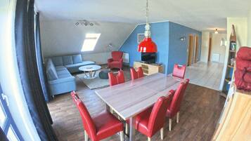 Een eethoek met een houten tafel en rode stoelen, een blauwe bank en een rode hanglamp.
