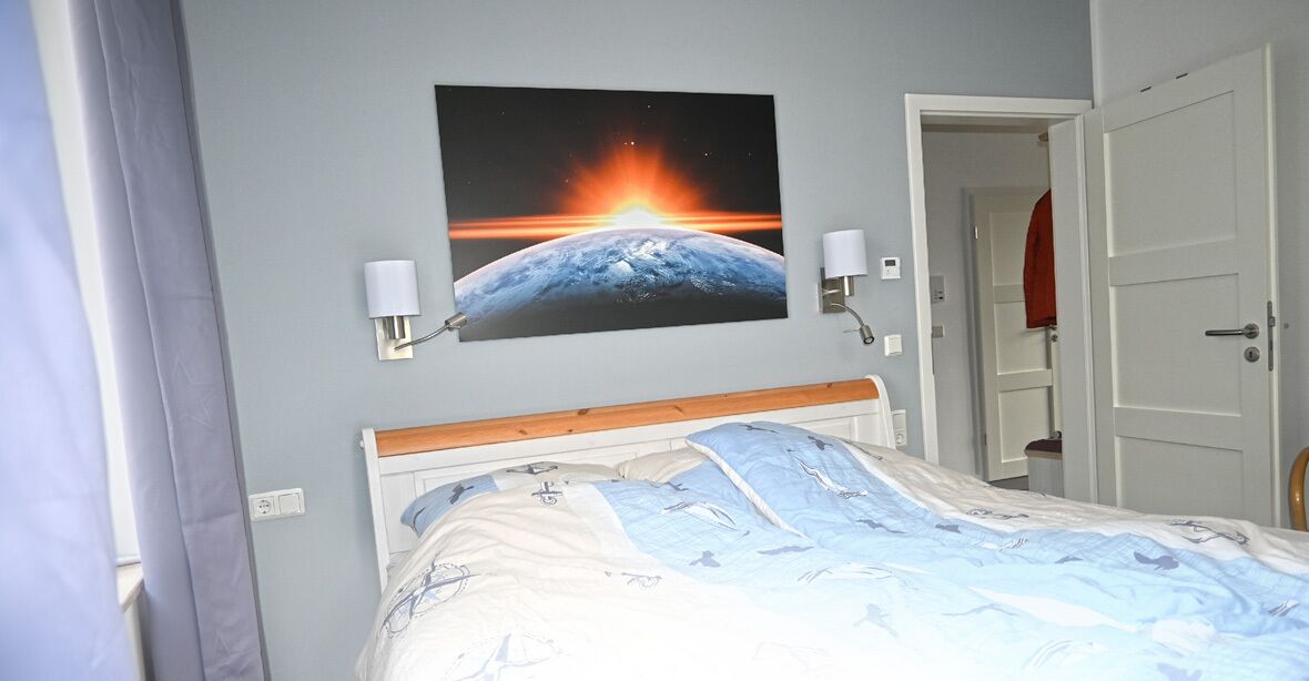 Un dormitorio con una cama, un cuadro de un planeta colgado en la pared y dos lámparas de pared.