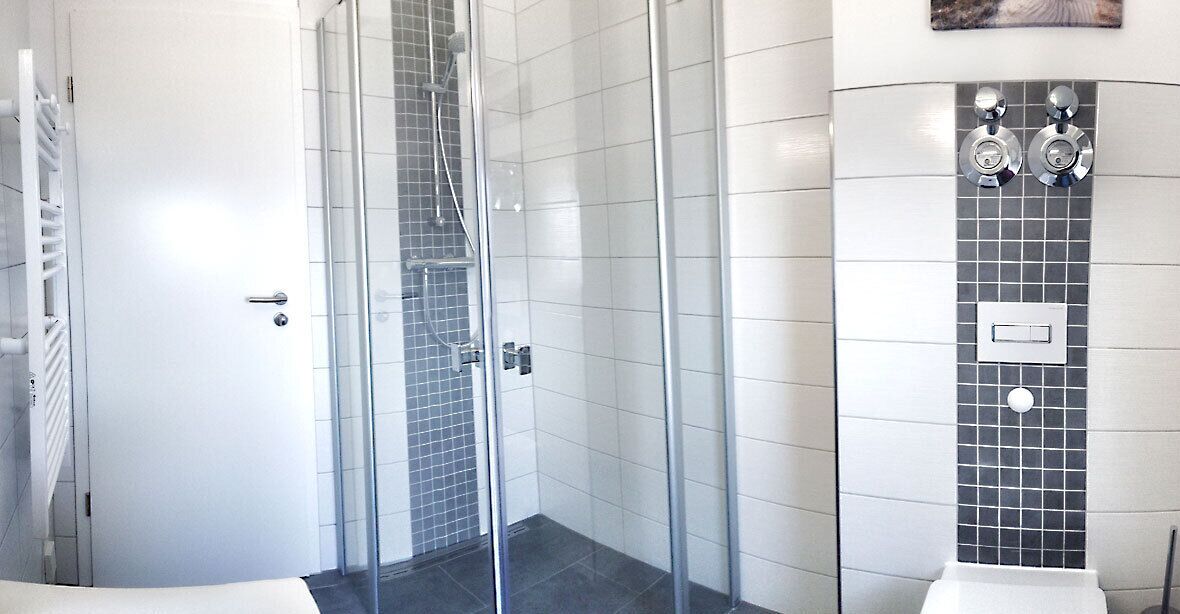 A modern bathroom with a glass shower enclosure, white tiled walls, and a white sink.