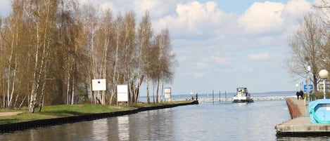 A calm river with a dock, trees, and a distant boat.