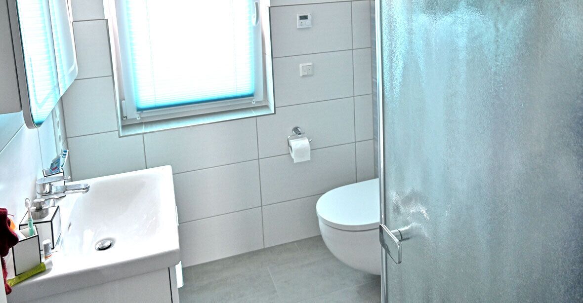 Un baño con lavamanos blanco, inodoro y una ventana sobre el lavamanos.
