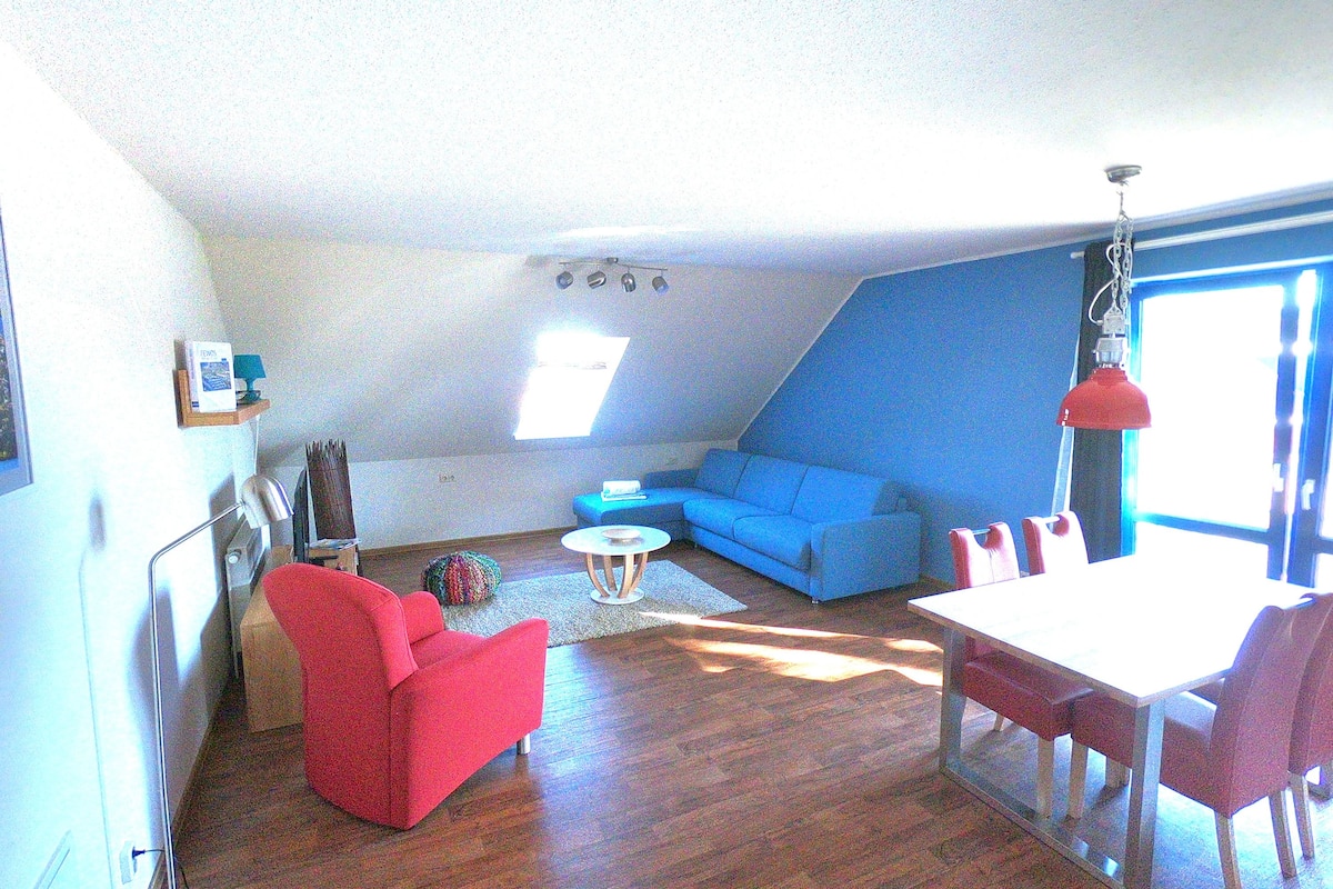 A living room with a blue sofa, red armchair, and a dining table with chairs.
