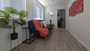 Een moderne woonkamer met een zwarte bank, een rode plaid en een grote potplant.