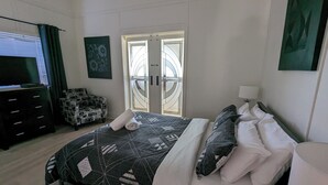 Een slaapkamer met een bed, een stoel, een televisie en een deur met een ruit.