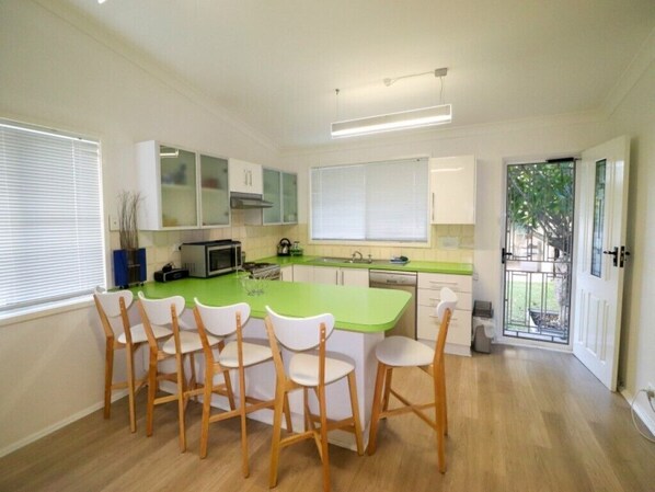 A modern kitchen with a green island, white cabinets, and wooden chairs. - Waterside Retreat @ Blacksmiths Beach (Blacksmiths)