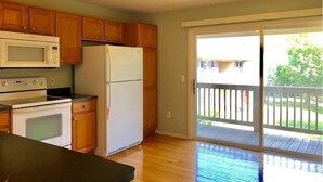A kitchen with wooden cabinets, a white refrigerator, a microwave, and an oven. There is a sliding glass door leading to a balcony. - Shanina Condo.. suit (Carroll)