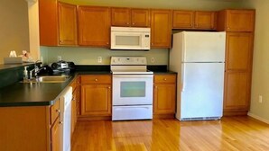 A kitchen with wooden cabinets, a microwave, a stove, and a refrigerator. - Shanina Condo.. suit (Carroll)